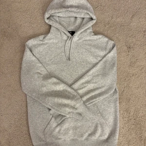 Grå hoodie från H&M Relaxed Fit XS/S - Snygg ljusgrå hoodie från H&M i relaxed fit. Tröjan har huva med snörning, magficka och långa ärmar. Perfekt för chill dagar och enkel att matcha med jeans eller joggers. Mjuk och skön bomullsblandning.funkar för S också 