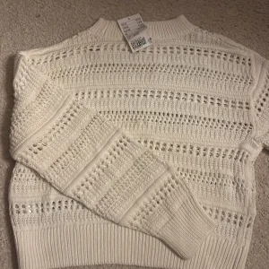 Vit stickad tröja med hålmönster - Säljer en vit stickad tröja med snyggt hålmönster och ribbade muddar. Tröjan har rund hals och lång ärm, perfekt för dig som gillar en klassisk men trendig look. Passar till många olika outfits och är supermjuk och skön.