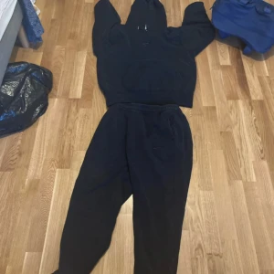 Svart Nike Air hoodie o byxor med huva M - Svart hoodie från Nike Air med broderad logga på bröstet och stor känguruficka. Tröjan har huva med snörning och är tillverkad i mjuk bomullsblandning. Perfekt för chill eller träning, loose fit och klassisk streetstyle.