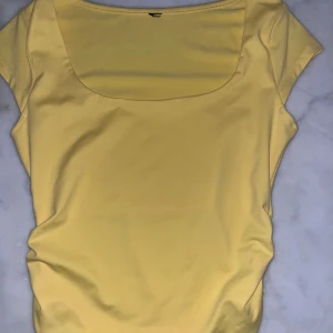 Gul topp med fyrkantig ringning - Snygg gul topp med korta ärmar och fyrkantig ringning. Väldigt skönt material och tajt. Storlek S men passar XS. Har klippt bort lappen men kommer ihåg att den är från Gina. 