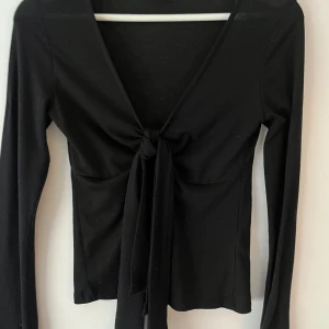Svart långärmad topp med knyt från Gina Tricot - Säljer Gina Tricot topp som inte kommer till användning! Inga slitningar men finns tecken av användning 