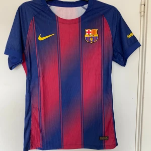 FC Barcelona Nike matchtröja M - Säljer en officiell FC Barcelona matchtröja från Nike i storlek M. Tröjan har klassiska blå och röda vertikala ränder, klubbmärke på bröstet och gula detaljer. Tillverkad i lätt Dri-FIT ADV-material som andas. Perfekt för dig som älskar Barca och vill ha en äkta supportertröja.