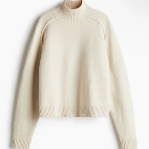 Beige stickad polotröja - Mysig beige stickad polotröja med ribbade muddar och hög krage. Perfekt för kyliga dagar och enkel att matcha med jeans eller kjol. Tröjan har en loose passform och långa ärmar för extra komfort.