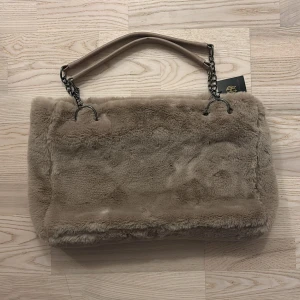 Beige pälsväska House of Harlow🤎 - Supermjuk och fluffig beige axelväska från House of Harlow. Väskan har pälsimitation, kedjedetaljer och ett brett handtag i beige skinnimitation. Stängs med dragkedja och har flera innerfack för småsaker. Ny med tag. 
