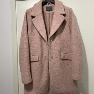 Rosa kappa från ICHI i storlek 38 - Säljer en snygg rosa kappa från ICHI i storlek 38. Jackan har en oversized look, bred krage och två fickor framtill. Materialet är ullmix med en mjuk, lite fluffig yta och insidan är fodrad i satin. Perfekt för höst och vinter!