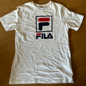 Vit Fila t-shirt - Vit t-shirt från Fila med stor, ikonisk logga i rött och marinblått på bröstet. 