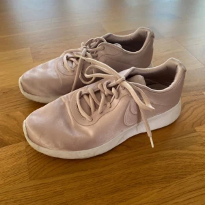 Ljusrosa Nike sneakers strl 38 - Säljer ett par ljusrosa Nike sneakers med klassisk logga på sidan. Skorna har snörning, rund tå och vit platt sula. Ovandelen är i syntetmaterial med en satinlik finish som ger en snygg look. Är inte använda så många gånger. 