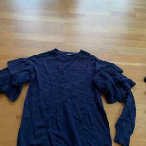 Mörkblå tröja med volangärmar - Säljer en mörkblå långärmad tröja med volangdetaljer på ärmarna. Tröjan har en  rund halsringning och har ett mjukt material.