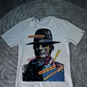 Billy jack tröja  - säljer en vit t-shirt från M.P.R med en stor färgstark Billy Jack grafik framtill. med blandade texter på tröjan, Riktig snygg och utstickande Billy Jack tröja 