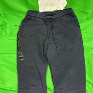 Svarta mjukisbyxor från Nike - Svarta mjukisbyxor från Nike med dragsko i midjan och diskret logga på låret. Byxorna har dragkedja vid fickorna och är tillverkade i mjukt material som passar perfekt för chill eller träning. Snygg, modern passform med paneldetaljer på benen.Liknande modell som originalet!