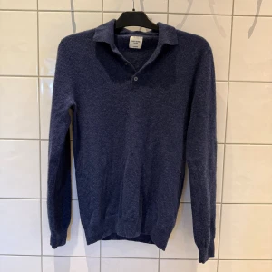 Blå pikétröja i 100% kashmir från John Henric - Blå pikétröja i 100% kashmir från John Henric. Tröjan har klassisk krage, knäppning med tre knappar och långa ärmar. Tröjan är i mycket bra skick, och den har alltid handtvättats och borstats med John Henric kashmir kam. Nypris: 2799 kr, Mitt pris: 800 kr