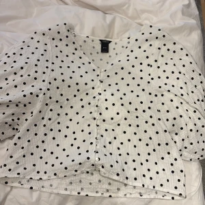 Vit prickig blus från Lindex - Supersöt vit blus från Lindex med svarta prickar, v-ringning och knappar framtill. Blusen har puffiga, trekvartsärmar och är tillverkad i ett lätt bomullstyg med diskreta ränder. Säljer den pgr av att den tyvärr är för stor för mig 