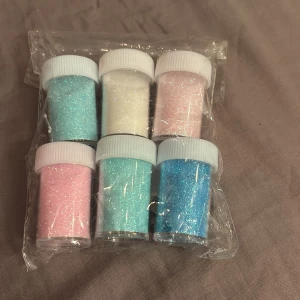 Set med pastellfärgat glitter - Sex burkar med superfint glitter i pastellfärger: ljusblått, vitt, ljusrosa och turkost. Perfekt för att skapa kreativa sminklooks eller använda som ögonskugga. Kommer i små plastburkar med vita skruvlock.