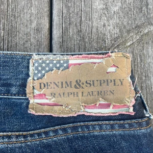 Ralph Lauren Denim & Supply Jeans - 33W 32L. Snygga blå jeans från Denim & Supply Ralph Lauren med klassisk femficksdesign med skön fade och honeycombs. Jeansen har en rak passform och detaljer som kontrastsömmar och patch med amerikansk flagga på backpatchen. 