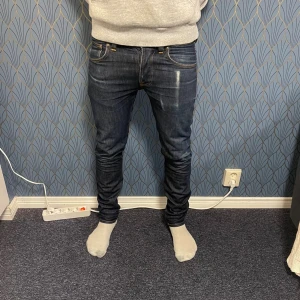 Mörkblå jeans från Nudie Jeans Co - Snygga mörkblå jeans från Nudie Jeans Co med klassisk femficksdesign och kontrastsömmar. Jeansen har en slim passform och raka ben, tillverkade i slitstarkt denimtyg av bomull. Perfekta för dig som gillar stilrena och tidlösa jeans. Storleken är W 31 och L34