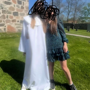 Blommig kortklänning med volang - Supersöt kort klänning i mörkblått och grönt med blommigt mönster. Klänningen har långa puffärmar, v-ringning med knyt och volangdetaljer nertill. Tillverkad i ett lätt, luftigt material som ger en flowy känsla. Perfekt för dig som vill sticka ut med en trendig look.