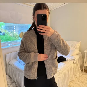 Beige teddyjacka från Dobber XS - Mysig beige teddyjacka från Dobber i storlek XS. Jackan har dragkedja framtill, två stora fickor och ribbade muddar vid ärmslut och midja. Perfekt för kyliga dagar när du vill vara både varm och snygg.