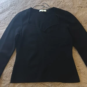 Svart långärmad topp med unik halsringning - Säljer en svart långärmad topp med en snygg och annorlunda fyrkantig halsringning. Toppen har en figurnära passform och är tillverkad i ett slätt material som ger en stilren look. Perfekt att styla med jeans eller tjol 
