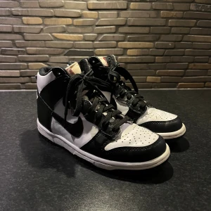Nike Dunk High svart/vit sneakers - Jag säljer mina Nike Dunk High sneakers i svart och vitt med klassisk Swoosh på sidan. Skorna har högt skaft, snörning och perforerad tå för extra ventilation. Varan har tecken på användning men har varit väl omhändertagen.