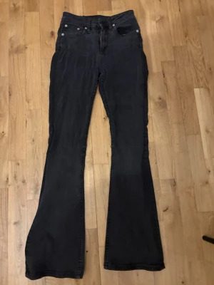 Svarta bootcut jeans med hög midja - Säljer ett par svarta jeans med bootcut-snitt och hög midja. Jeansen har klassiska fem fickor fram och två stora fickor bak. Materialet är jeans och färgen är mörk svart.                        Kostar lite pågrund av att vill få solt dom snabbt 