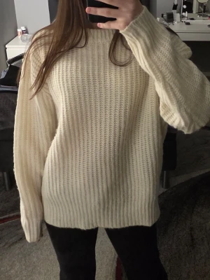 Krämvit stickad tröja från Lager 157 - Säljer en krämvit stickad tröja från Lager 157 med grovstickad struktur och rund hals. Tröjan har långa ärmar och bred ribbstickad mudd vid ärmslut och nederkant. Perfekt för lager på lager under kyliga dagar.