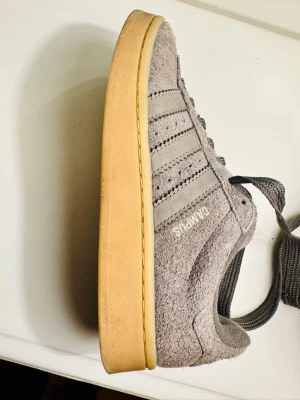 Grå adidas Campus sneakers mocka - Snygga grå adidas Campus sneakers i mocka med klassiska tre ränder på sidan och Campus-tryck i vitt. 