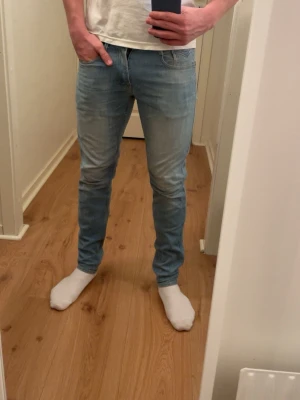 Ljusblå slim fit jeans herr - Säljer ett par ljusblå slim fit jeans med klassisk femficksdesign och normal midja. Jeansen har en snygg tvätt och smal passform som sitter tajt längs benen. Perfekta för en avslappnad och trendig look.