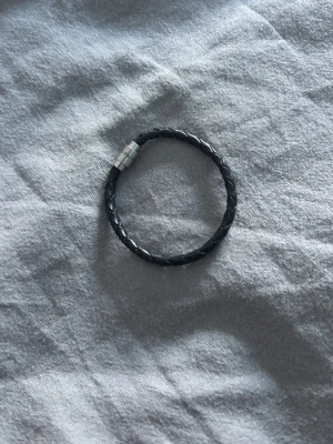 Svart läder armband. To the moon and back - Stilrent svart armband i flätat läder med ett magnetiskt lås i silverfärgad metall. Perfekt accessoar för en cool och enkel look. Passar både till jeans och skjorta. Kostar 339kr ny, säljer för 99kr