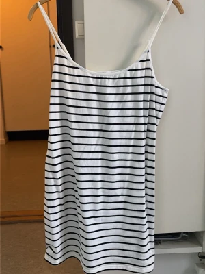 Randigt vitt nattlinne med smala axelband - Ett vitt nattlinne med svarta horisontella ränder och smala axelband. Mjuk och lätt bomullskänsla, perfekt för att chilla hemma eller sova i. Enkel och klassisk design med rak passform. Är lite liten i storleken.