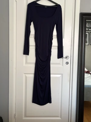 Marinblå långklänning med rynk - Snygg marinblå långklänning med lång ärm och rundad urringning. Klänningen har åtsittande passform och rynkade detaljer längs sidorna som ger en smickrande siluett. Perfekt för dig som gillar stilrena och eleganta plagg.