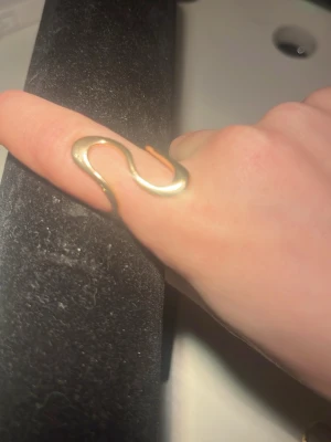 Guldig vågig ring i modern design - Säljer två snygga ringar  i guldtonad metall med en vågig, organisk form som slingrar sig runt fingret. Ringen har en minimalistisk och trendig look som sticker ut och passar perfekt för dig som gillar unika accessoarer.Två st båda går att köpa enskilt eller tsm. Ena är från Uropenn och andra HM