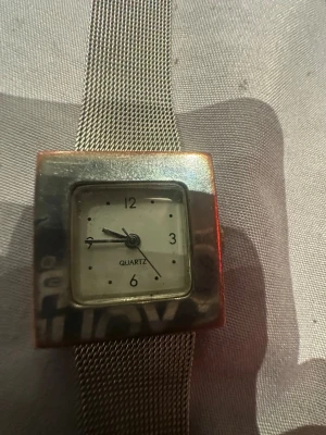 Silvrig fyrkantig mesh-klocka - Stilren klocka med fyrkantigt silvrigt ur och mesh-armband i metall. Urtavlan är vit med svarta siffror och markeringar. Klassisk quartz-urverk och enkel design som passar till det mesta. Funkar ej!