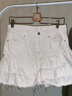 Vit volangkjol med fransig kant - Supersnygg vit kortkjol från Gina tricot original pris 400 med volanger och fransiga kanter. Kjolen har klassiska jeansfickor fram och bak samt knapp och dragkedja i midjan. Perfekt för dig som vill ha en cool och avslappnad stil.