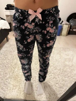 Mörkblå blommiga pyjamasbyxor - Pyjamasbyxor i mörkblått med blommor samt en  rosa rosett i midjan. Materialet är väldigt mjukt och behagligt. Från Kappahl, stl 170 men passar xs/s också🌸
