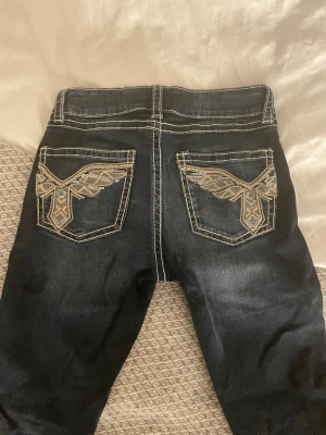 Mörkblå jeans med broderade fickor - Säljer mörkblå jeans med kontrastsömmar och broderade bakfickor i guld och silver. Från Gina Tricot i storlek 164.