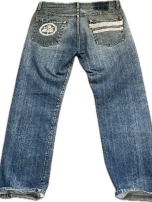 Momotaro Jeans – Selvedge Denim – Made in Japan - A pair of stunning high-quality Momotaro Jeans made in Okayama, Japan. Features the iconic "Going to Battle" stripes on the back pocket and beautiful selvedge detailing. Great condition with authentic patina and character. Feel free to message me if you have any questions! • Waist: 44 cm • Thigh: 31 cm • Inseam: 78 cm • Total Length: 105 cm • Leg Opening: 22 cm 