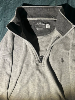 Grå halvzip-tröja från Polo Ralph Lauren - Snygg grå långärmad tröja från Polo Ralph Lauren med halv dragkedja och broderad logga på bröstet. Mjuk bomullsblandning och hög krage som går att vika ner. Perfekt för lager-på-lager och chill stil. Sick 9/10. Pris kan diskuteras.