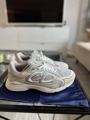 B30 sneakers DIOR - Säljer ett par Dior B30 sneakers i vit färg. Skorna är i storlek 43 och i mycket fint skick. De är oanvända, dock finns en mindre fläck på ena skon (se bilder). Originalsnören medföljer. Observera att ingen box eller dustbag ingår.