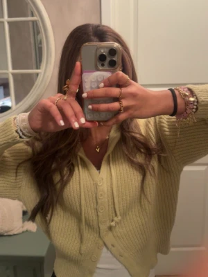 Ljusgul ribbstickad hoodie - Säljer en ljusgul ribbstickad croppad ”hoodie” med v-ringning och knappar framtill. Koftan har en avslappnad passform och långa ärmar, perfekt att slänga över en topp. Materialet är mjukt och bekvämt, och färgen är superfräsch. Köpt från NA-KD för länge sen och har använt den ett fåtal gånger 