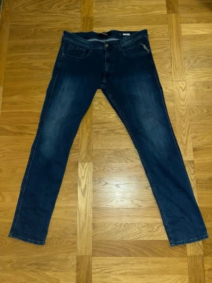 Blå Replay Anbass jeans herr - Säljer ett par klassiska blå Replay Anbass jeans med fem fickor och snygga slitningar. Jeansen har normal form med slim fit passform, tillverkade i mjuk bomullsdenim med stretch för extra komfort. Dem är helt oanvända men saknar lapparna. Passar en person som är mellan 175-190 cm.