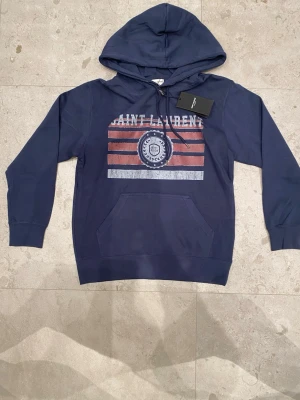 Saint Laurent hoodie – helt ny – strl S - Säljer en Saint Laurent hoodie i storlek S. Den är helt ny och oanvänd, lappen sitter kvar.  Jag har tyvärr ingen djupare kunskap om Saint Laurent och kan därför inte garantera äkthet, säljs som helt ny.  Mitt pris: 1 599 kr Nypris: ca 10 000 kr  Vänliga hälsningar, Stylespotresell