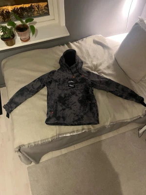 Svartgrå vindjacka från Dope - Snygg svartgrå vindjacka från Dope med tie-dye mönster och stor huva. Jackan har en praktisk magficka med DOPE-logga och dragsko i huvan med orange detaljer. Perfekt för dig som vill ha en streetstyle-look och gillar funktionella detaljer.