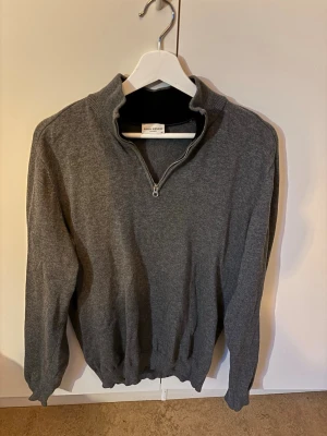 Grå halvzip tröja John Henric - Mörkgrå tröja från John Henric med halvzip och hög krage. Tillverkad i mjukt material, perfekt för lager på lager. Klassisk och stilren design med ribbade muddar vid ärmslut och nederkant.