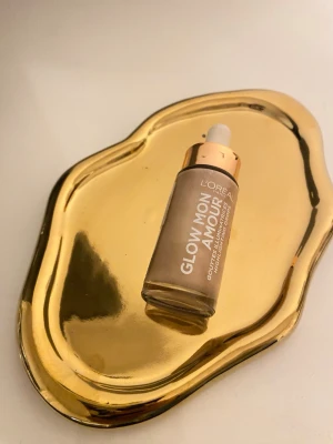 L'Oréal Glow Mon Amour highlighter - Flytande highlighter från L'Oréal i nyansen Glow Mon Amour. Kommer i en glasflaska med pipett och har ett skimrande, champagnefärgat glow. Perfekt för att ge huden en fräsch och strålande finish. Snygg och lyxig förpackning med gulddetaljer.
