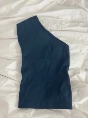 Mörkblå one shoulder topp från Zara - Snygg mörkblå one shoulder topp från Zara. Toppen är ärmlös och har en stilren, tight passform som framhäver axeln. Perfekt att styla med jeans eller kjol för en trendig look.