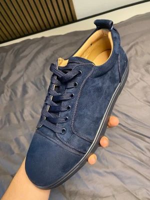 Mörkblå sneakers i mocka - Stilrena mörkblå sneakers från Christian Louboutin i mjuk mocka med matchande blå snörning och diskret broderad logga på hälen. Skon har en låg profil och en mörk sula som ger en clean look. Insidan är ljusbeige för extra kontrast.