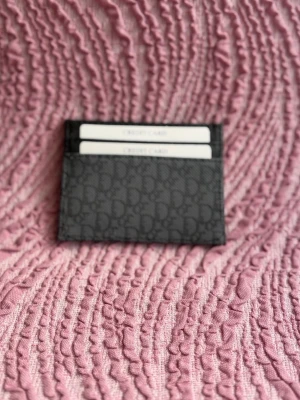 Svart  korthållare i monogram - Snygg svart korthållare f med klassiskt monogrammönster. Plats för flera kort och smidig att ha i fickan. Perfekt accessoar för dig som gillar stilrena detaljer och designerplagg.