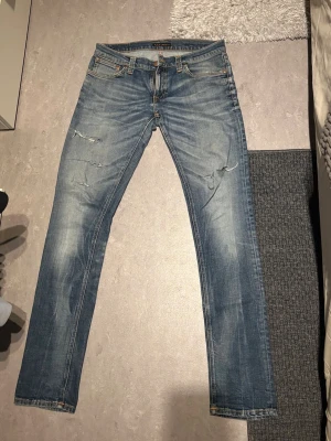 Blå slitna jeans från Nudie Jeans - Säljer ett par riktigt snygga blå jeans från Nudie Jeans med snygga slitningar och ljusa partier. Stl w32 l34. Smala i modellen. 