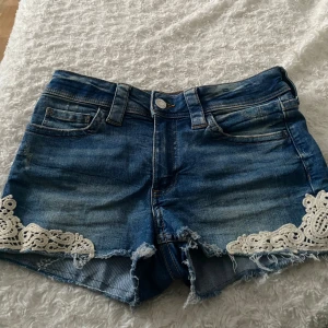 Blå jeansshorts med spetsdetaljer - Snygga blå jeansshorts med råa kanter och vita spetsdetaljer längst ner på benen från H&M