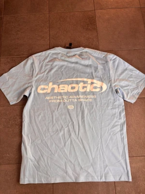 Ljusblå t-shirt med tryck - Snygg ljusblå t-shirt från Chaotic med vitt tryck både fram och bak. Oversized passform och klassisk rund hals. Perfekt för dig som gillar streetwear och vill sticka ut med ett coolt statement-plagg.